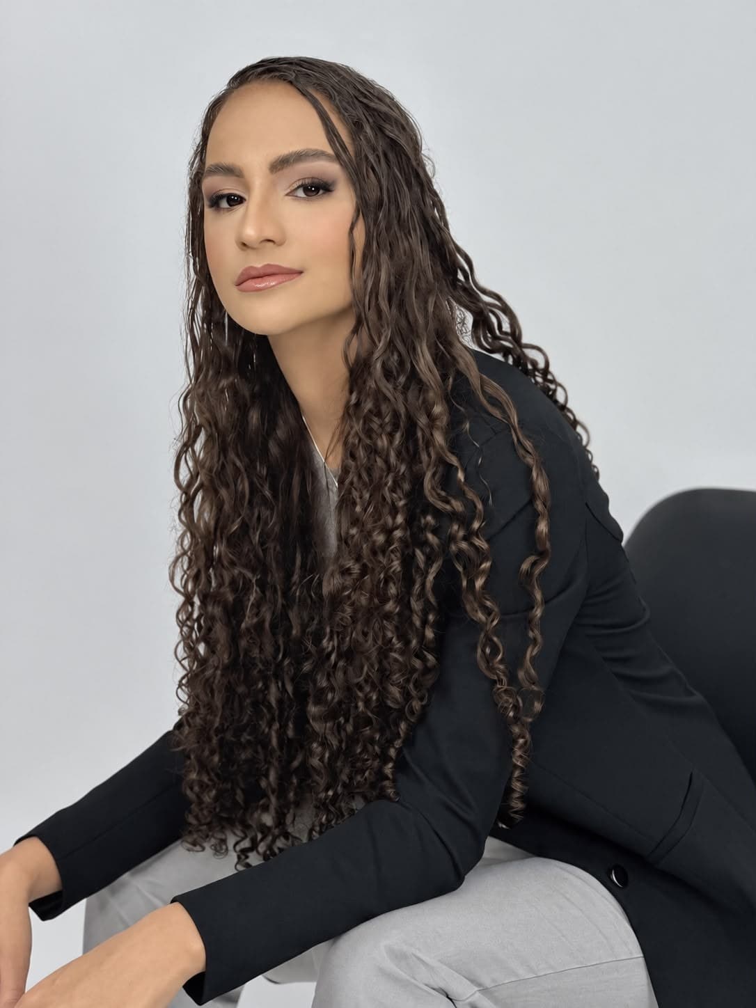 Luiza Pego sentada, de blazer preto, com os cabelos cacheados longos soltos